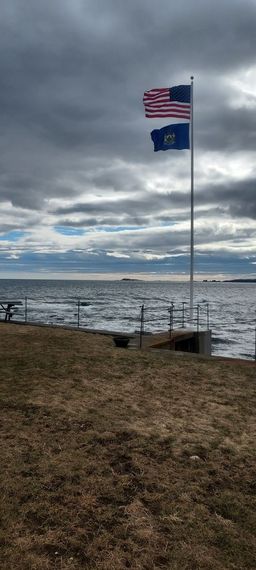 Maine state flag flying over the shore under a grey sky