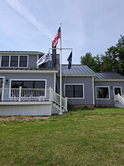 Yardarm flagpole beside a shorefront home flying multiple flags