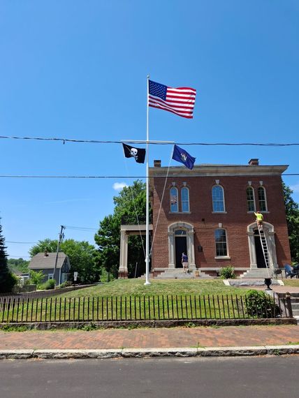 Technician on a ladder servicing a yardarm flagpole at a brick municipal building