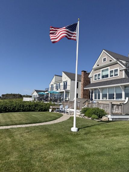 White fiberglass flagpole on the lawn of a shingle-style coastal home