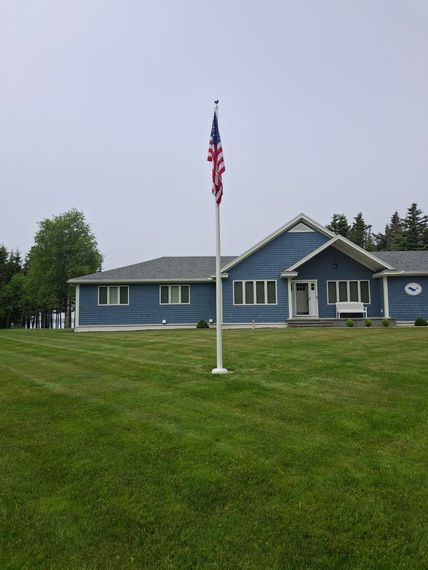 Flagpole on a wide lawn in front of a blue Maine home
