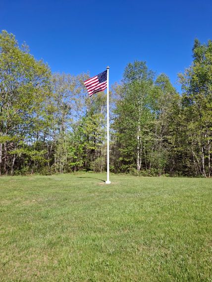Flagpole on a mown lawn at the edge of the treeline